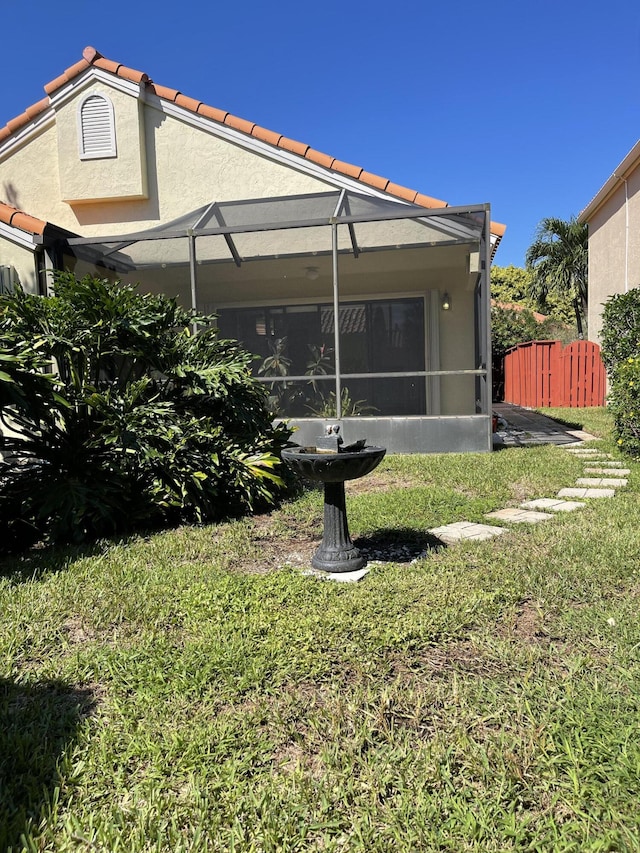 rear view of property featuring glass enclosure and a lawn