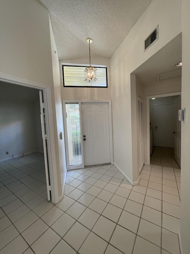 entrance foyer featuring light tile patterned floors, a textured ceiling, high vaulted ceiling, and a chandelier