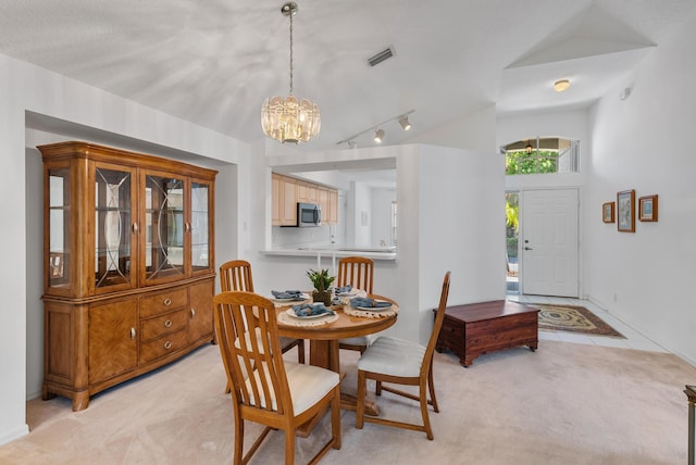 dining area with a chandelier, rail lighting, light colored carpet, and vaulted ceiling