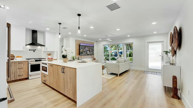 kitchen with high end white range oven, white cabinets, wall chimney range hood, hanging light fixtures, and light hardwood / wood-style flooring