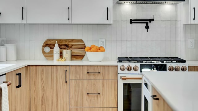 kitchen featuring white cabinets, high end stove, backsplash, and extractor fan