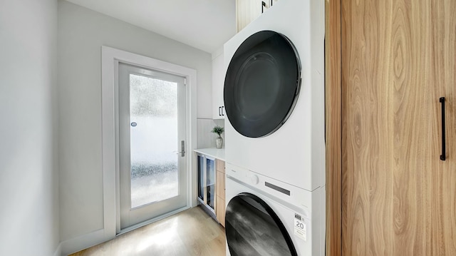 laundry area featuring stacked washer / drying machine, a healthy amount of sunlight, and light hardwood / wood-style floors