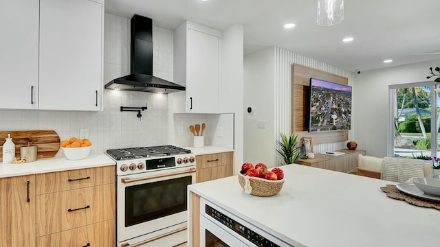 kitchen featuring high end stove, white cabinets, decorative backsplash, and wall chimney exhaust hood