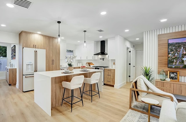 kitchen featuring light wood-type flooring, white appliances, wall chimney range hood, pendant lighting, and white cabinetry