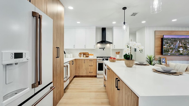 kitchen with white cabinetry, wall chimney range hood, high end white range oven, refrigerator, and pendant lighting