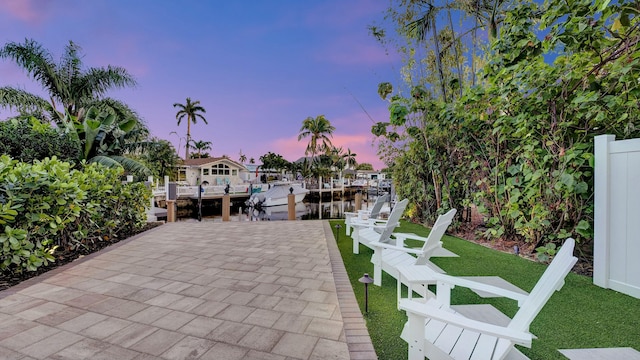 patio terrace at dusk featuring a lawn, a dock, and a water view