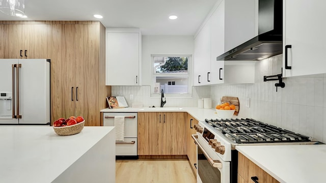 kitchen featuring white appliances, backsplash, white cabinets, wall chimney range hood, and sink