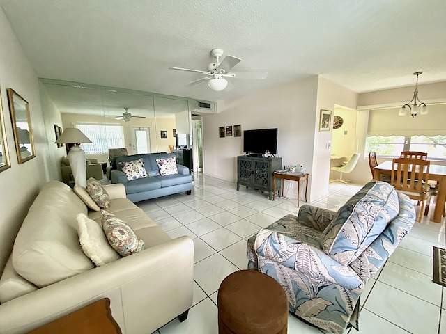 living room featuring a textured ceiling, light tile patterned floors, and ceiling fan with notable chandelier