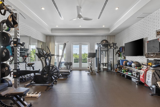 gym with french doors, a tray ceiling, ceiling fan, and brick wall