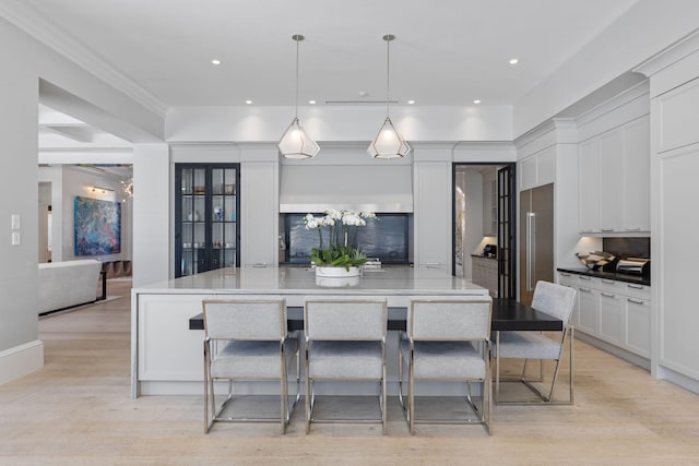 kitchen with a large island, light stone counters, decorative light fixtures, a kitchen bar, and white cabinets