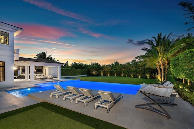 pool at dusk with a lawn, a patio area, and outdoor lounge area