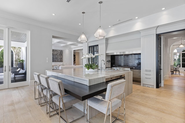 kitchen featuring pendant lighting, backsplash, a large island with sink, white cabinets, and light stone countertops