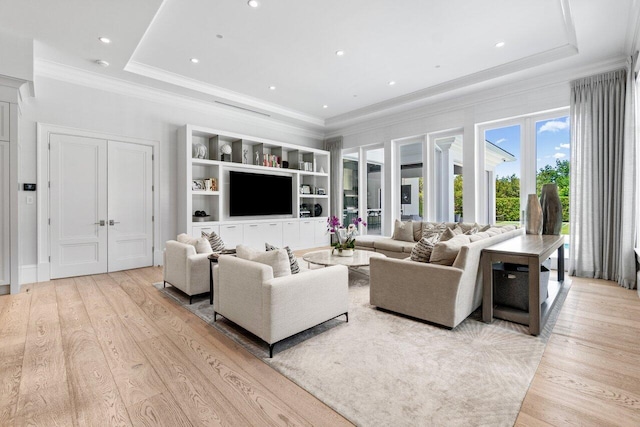 living room with light wood-type flooring, a raised ceiling, and crown molding