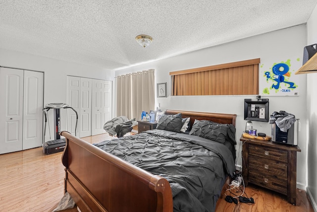 bedroom featuring two closets, a textured ceiling, and light hardwood / wood-style flooring