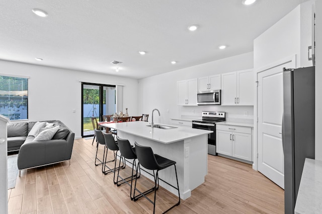 kitchen featuring appliances with stainless steel finishes, sink, a center island with sink, white cabinetry, and a breakfast bar area