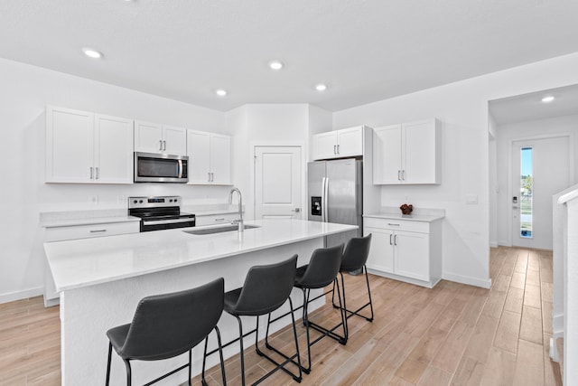 kitchen featuring a breakfast bar, stainless steel appliances, a kitchen island with sink, sink, and white cabinets