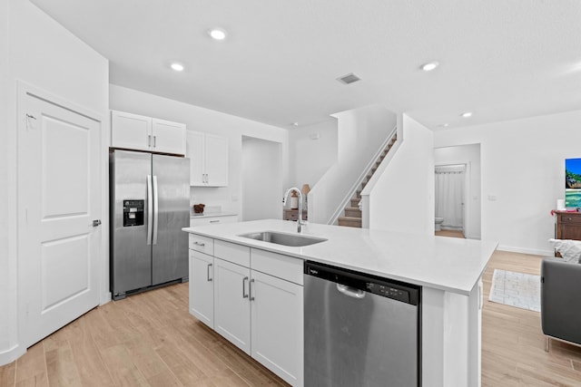 kitchen with white cabinetry, sink, stainless steel appliances, a kitchen island with sink, and light wood-type flooring