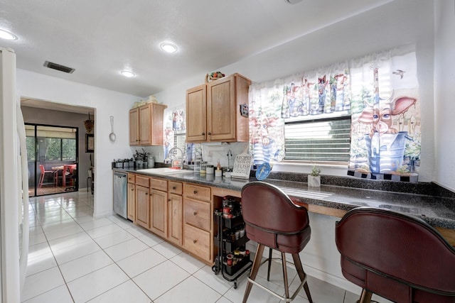 kitchen featuring sink, stainless steel dishwasher, white fridge, a breakfast bar area, and light tile patterned floors