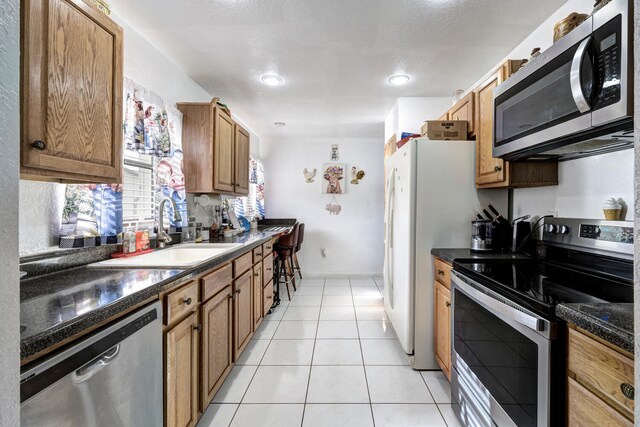 kitchen featuring light tile patterned floors, stainless steel appliances, dark stone countertops, and sink