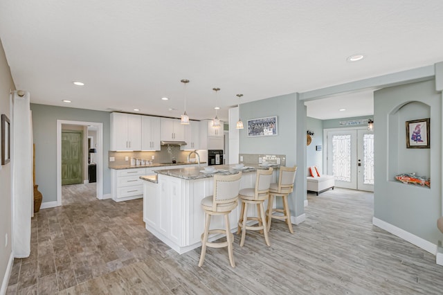 kitchen with white cabinets, french doors, hanging light fixtures, oven, and light stone counters