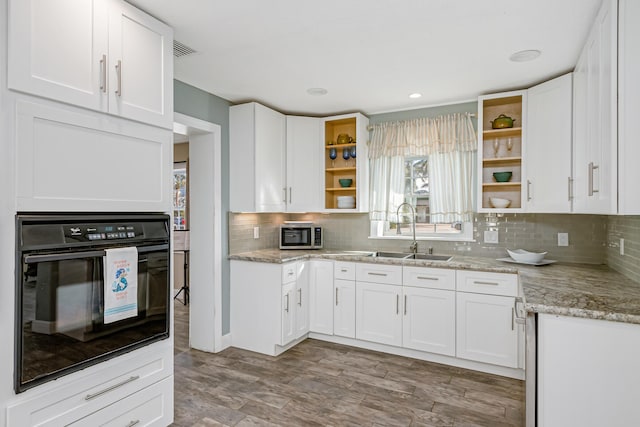 kitchen with light hardwood / wood-style flooring, black oven, white cabinets, light stone counters, and sink