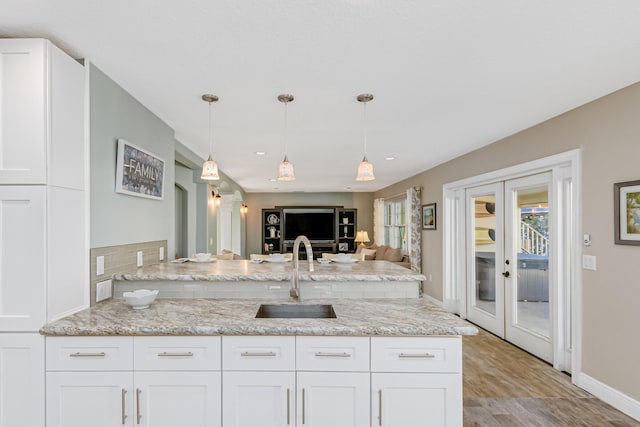 kitchen featuring white cabinetry, decorative light fixtures, french doors, light stone counters, and sink