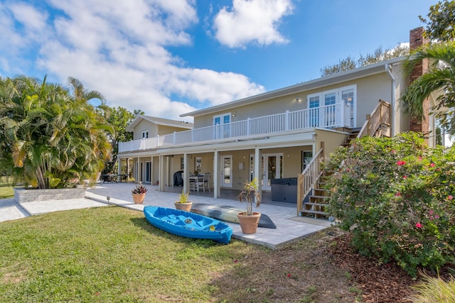 back of house with a balcony, a hot tub, french doors, a patio, and a yard