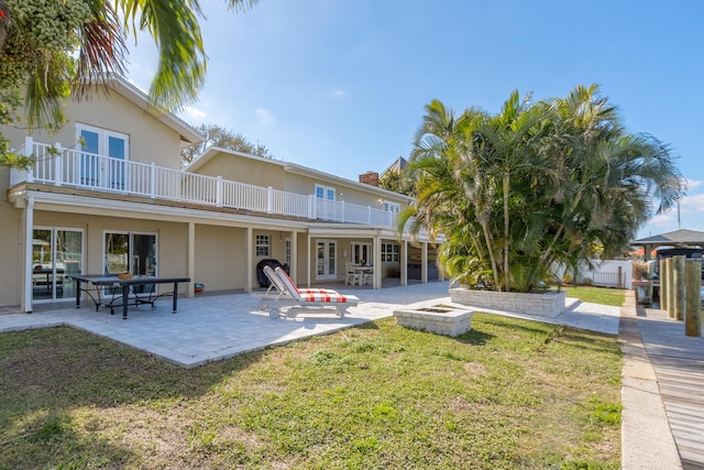 back of property with a lawn, an outdoor fire pit, a patio area, and a balcony