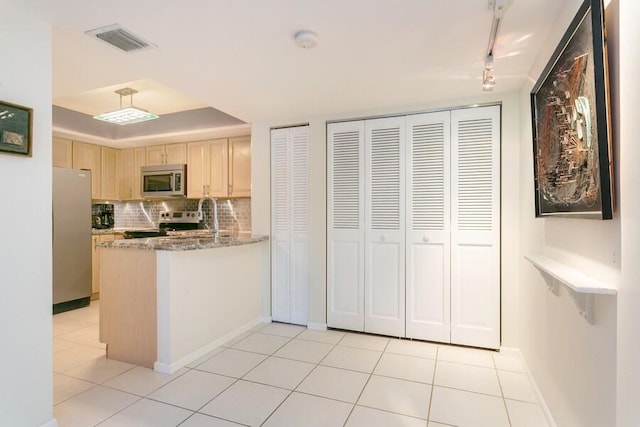 kitchen featuring appliances with stainless steel finishes, stone counters, light brown cabinetry, kitchen peninsula, and decorative backsplash