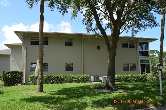 rear view of property with central air condition unit and a lawn