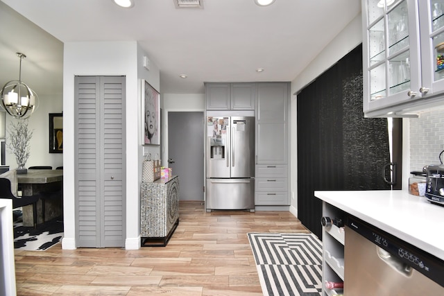 kitchen featuring decorative backsplash, gray cabinetry, stainless steel appliances, a chandelier, and hanging light fixtures