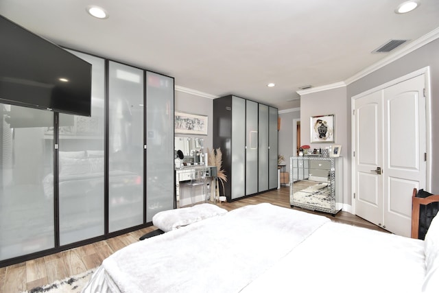 bedroom with wood-type flooring, ornamental molding, and two closets