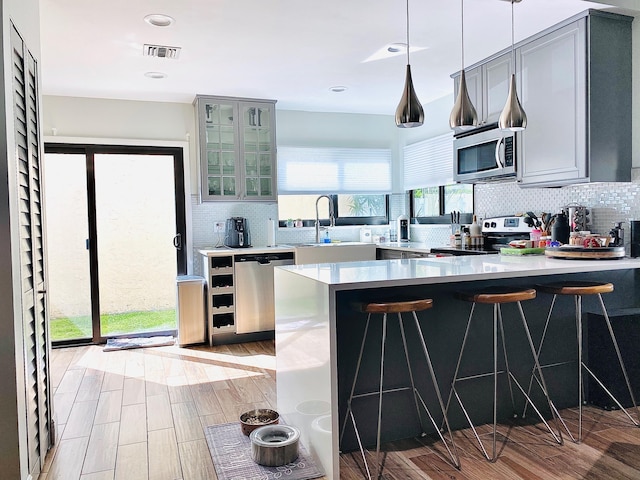 kitchen with backsplash, sink, appliances with stainless steel finishes, decorative light fixtures, and kitchen peninsula