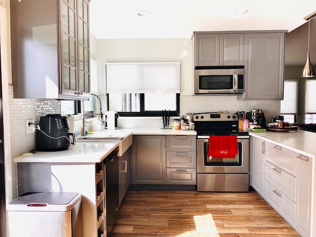 kitchen with gray cabinetry, sink, stainless steel appliances, and decorative light fixtures