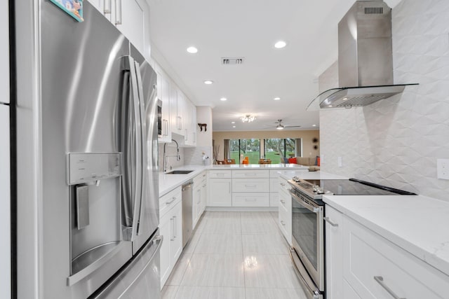 kitchen with white cabinets, appliances with stainless steel finishes, sink, and wall chimney range hood