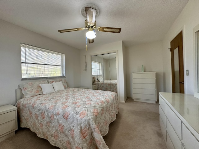 bedroom with a textured ceiling, a closet, ceiling fan, and light colored carpet