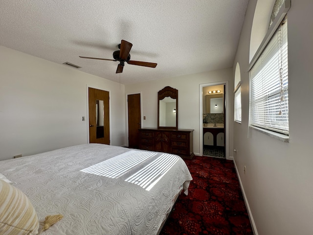 bedroom featuring a textured ceiling, ceiling fan, multiple windows, and ensuite bath