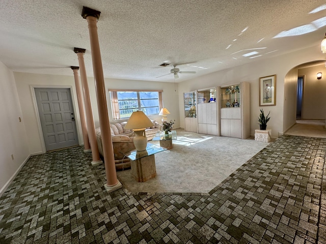 unfurnished living room with dark colored carpet, a textured ceiling, ornate columns, and ceiling fan