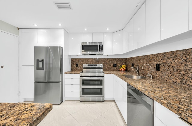 kitchen with dark stone counters, stainless steel appliances, sink, light tile patterned floors, and white cabinetry