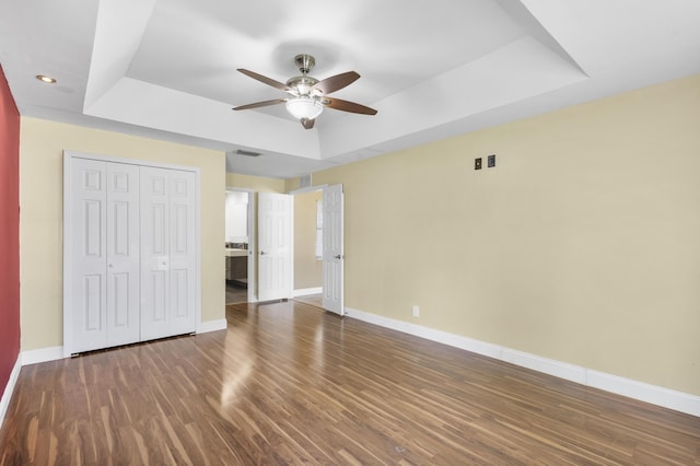 unfurnished bedroom featuring dark hardwood / wood-style flooring, a closet, a raised ceiling, and ceiling fan