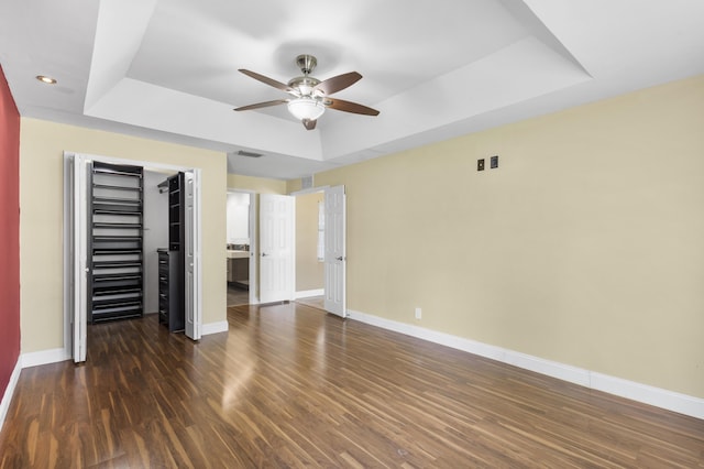 unfurnished bedroom featuring a raised ceiling, a closet, dark wood-type flooring, and ceiling fan