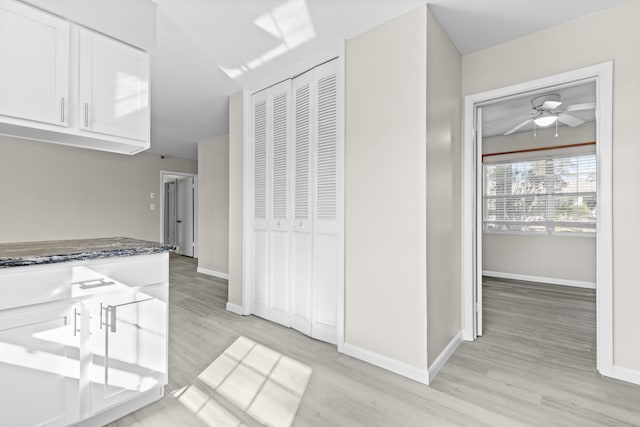 kitchen featuring ceiling fan, light wood-type flooring, white cabinetry, and dark stone counters