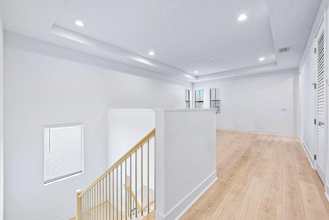 hallway with a tray ceiling and light wood-type flooring