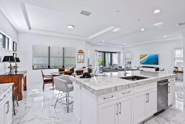 kitchen featuring a raised ceiling, a kitchen island with sink, sink, and white cabinets