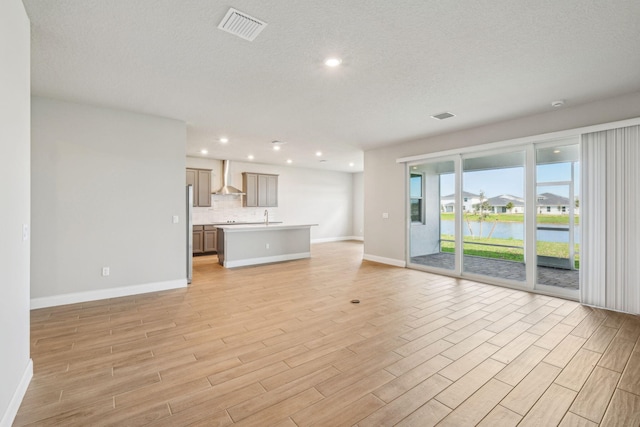 unfurnished living room with sink, light hardwood / wood-style flooring, a textured ceiling, and a water view