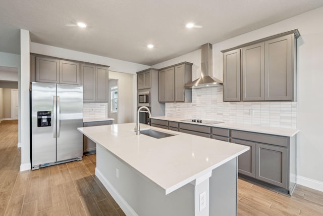 kitchen with sink, appliances with stainless steel finishes, gray cabinetry, a kitchen island with sink, and wall chimney exhaust hood