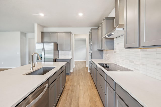 kitchen featuring wall chimney exhaust hood, sink, appliances with stainless steel finishes, gray cabinets, and light hardwood / wood-style floors