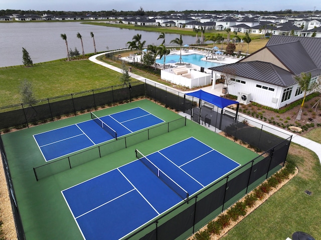 view of tennis court with a water view, a yard, and a fenced in pool