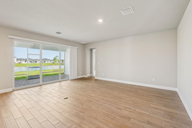 empty room featuring a water view, light hardwood / wood-style flooring, and a textured ceiling