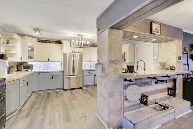 kitchen with white cabinetry, tasteful backsplash, light wood-type flooring, stainless steel refrigerator, and pendant lighting